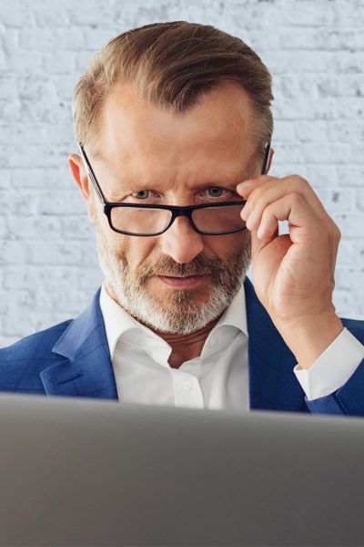 Man peers over the top of his glasses at computer