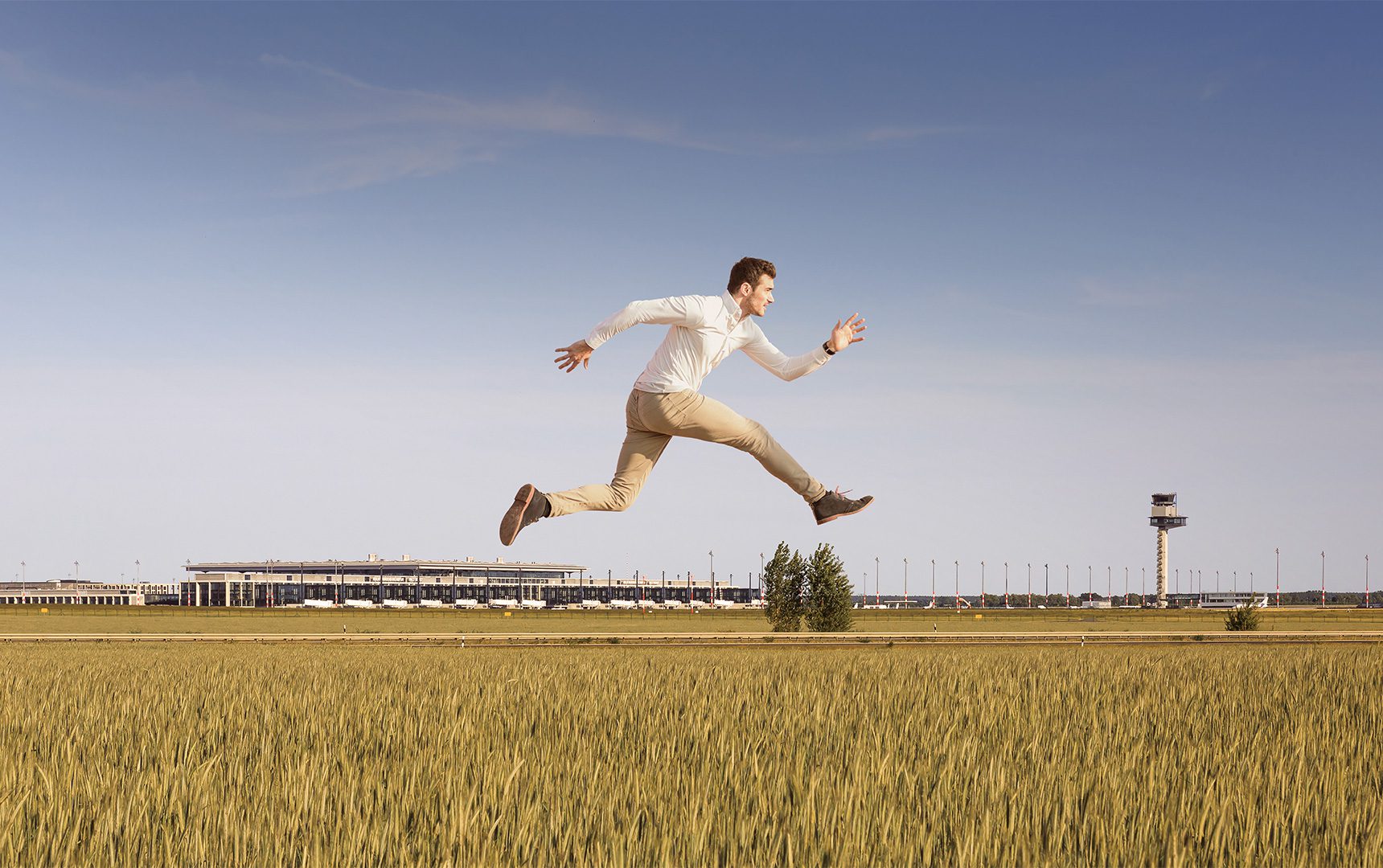 Man leaping over field with airport in the background