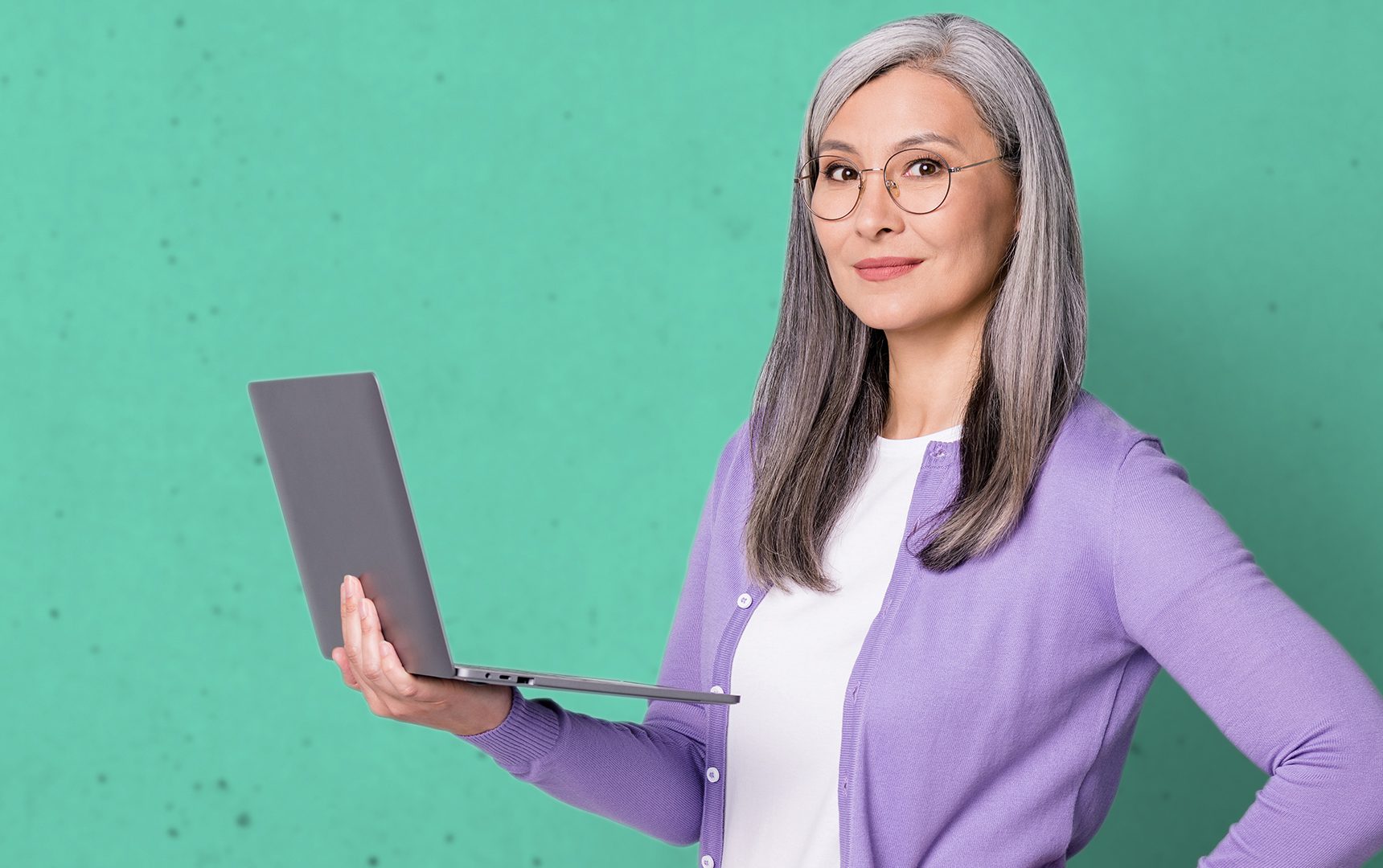 Woman smiling holding laptop in right hand against turquoise background