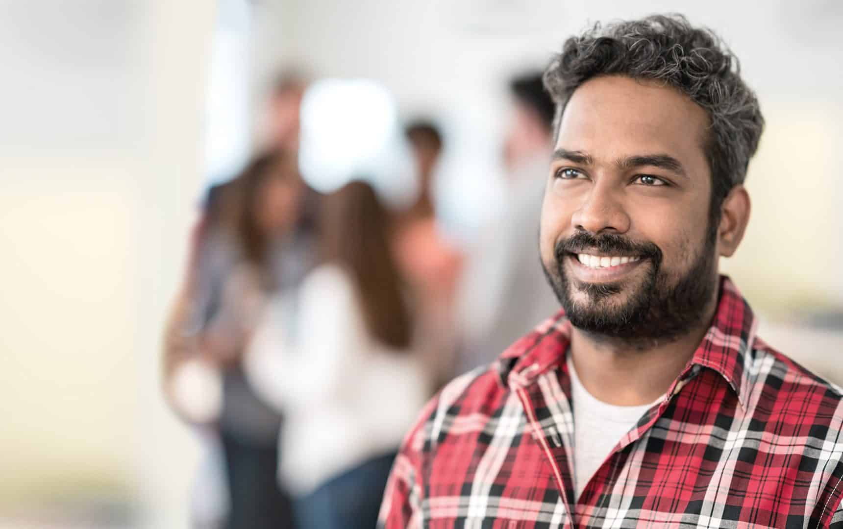 Man smiles in front of blurred background of colleagues