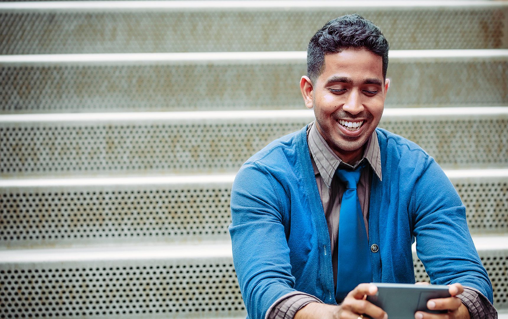 Man smiles at tablet while sitting on stairs