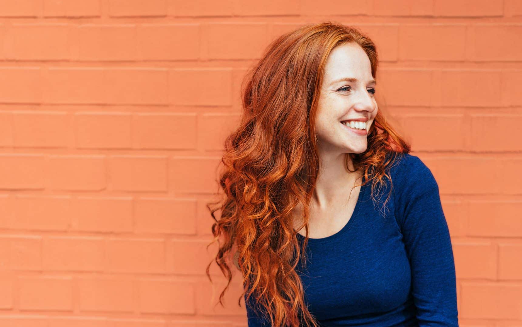 Woman smiling and looking right against an orange brick wall