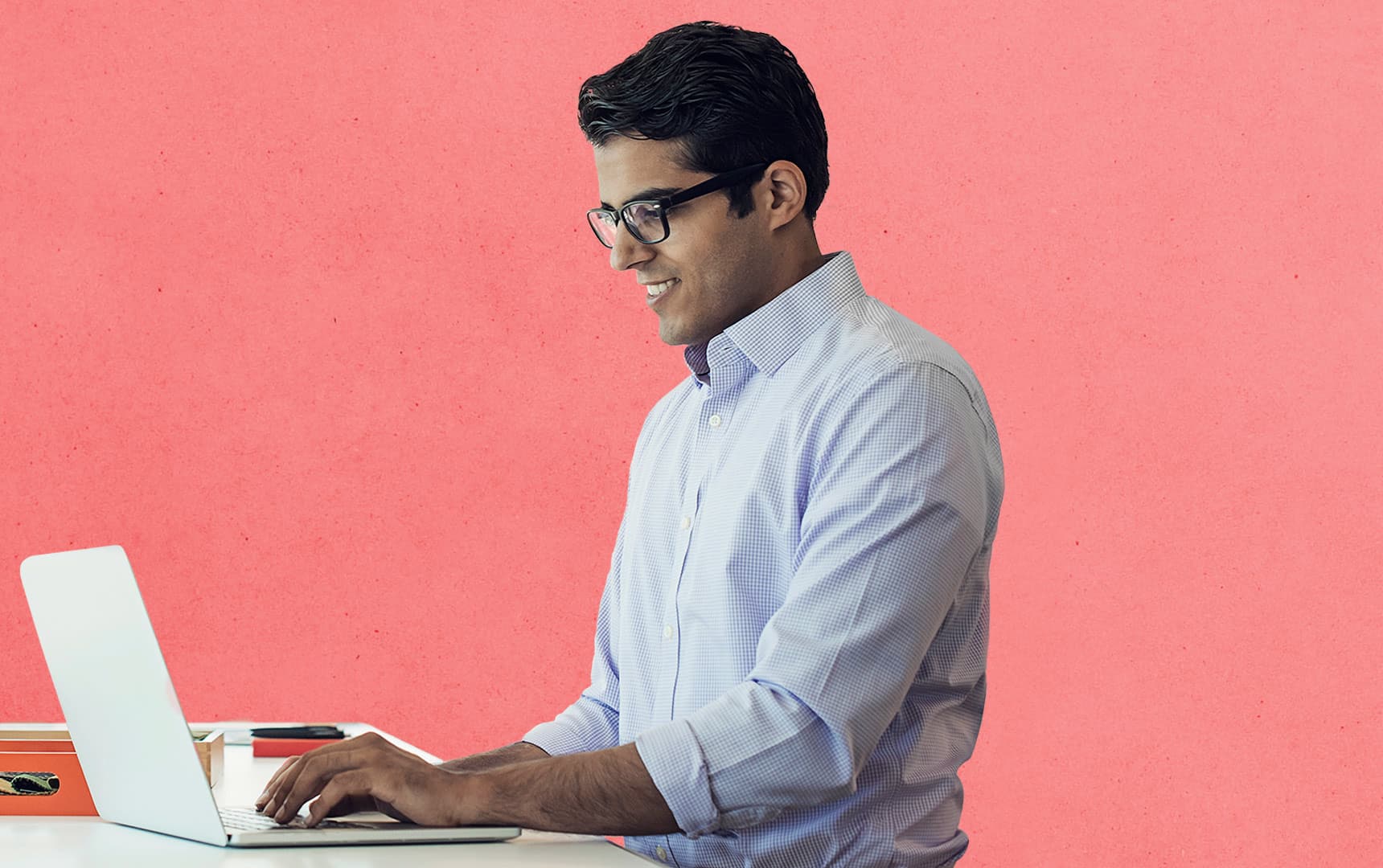 Man in glasses with pink background types on his laptop
