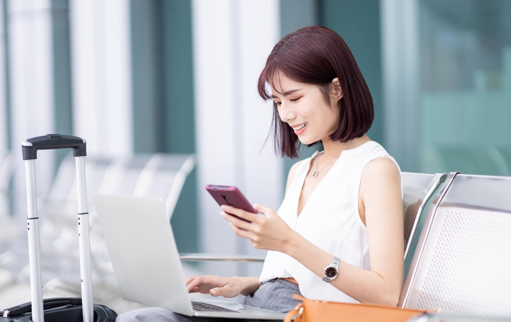 Woman sitting on workplace in front of laptop looking into her mobile phone